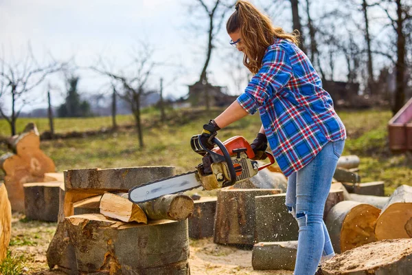 Young Woman using chainsaw to cut a log for firewood.