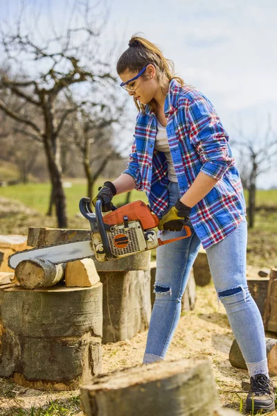 Young Woman using chainsaw to cut a log for firewood.