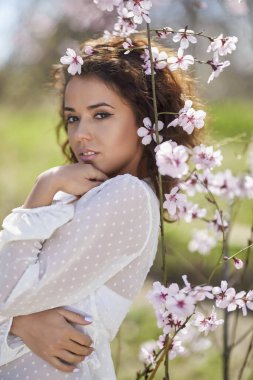 Ağaç çiçeklerinin yanında kıvırcık saçlı güzel bir kadının bahar portresi.