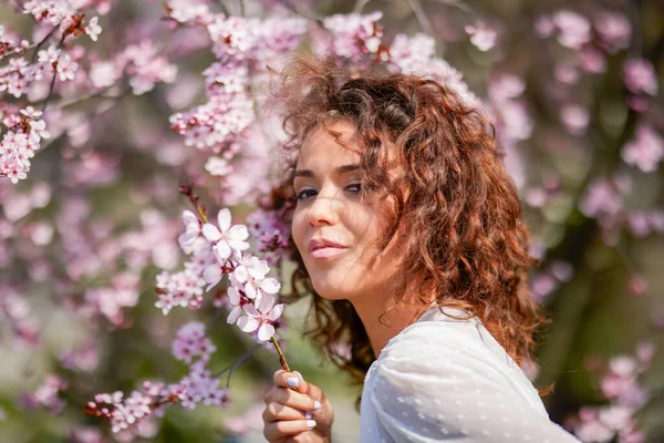 一个美丽的女人的春天肖像 她的卷曲的头发紧靠着树的花朵 — 图库照片