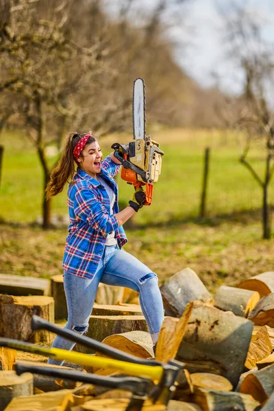 Young Woman using chainsaw to cut a log for firewood.