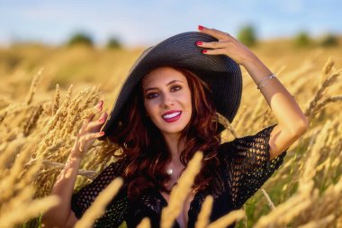 Gün batımında şapkalı güzel bir esmer kadın çimlerde poz verir..