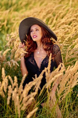 Gün batımında şapkalı güzel bir esmer kadın çimlerde poz verir..