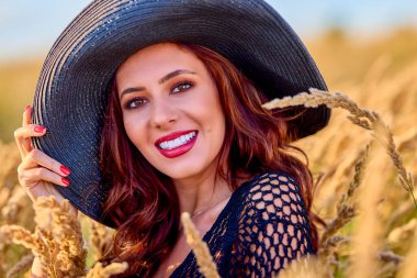 Gün batımında şapkalı güzel bir esmer kadın çimlerde poz verir..