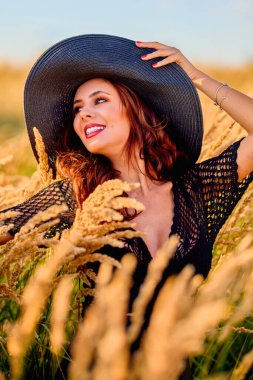 Gün batımında şapkalı güzel bir esmer kadın çimlerde poz verir..