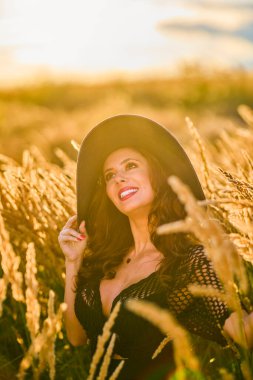 Gün batımında şapkalı güzel bir esmer kadın çimlerde poz verir..