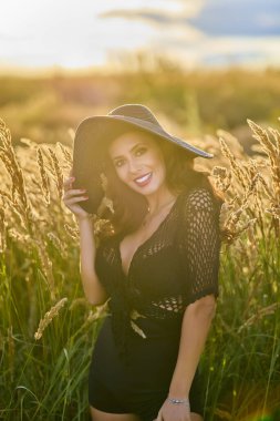 Gün batımında şapkalı güzel bir esmer kadın çimlerde poz verir..