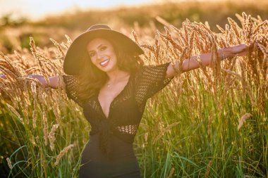 Gün batımında şapkalı güzel bir esmer kadın çimlerde poz verir..