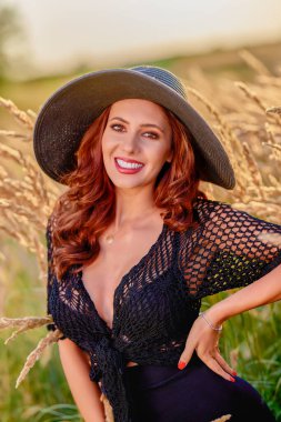 Gün batımında şapkalı güzel bir esmer kadın çimlerde poz verir..