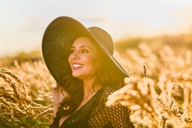 Gün batımında şapkalı güzel bir esmer kadın çimlerde poz verir..