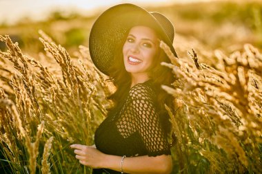 Gün batımında şapkalı güzel bir esmer kadın çimlerde poz verir..