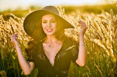 Gün batımında şapkalı güzel bir esmer kadın çimlerde poz verir..