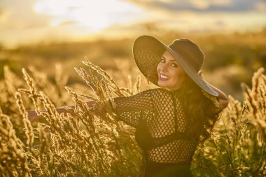 Gün batımında şapkalı güzel bir esmer kadın çimlerde poz verir..