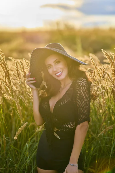 Gün batımında şapkalı güzel bir esmer kadın çimlerde poz verir..