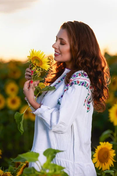 Beautiful woman enjoying nature in the sunflower field at sunset. Traditional clothes. Attractive brunette woman with long and healthy hair.