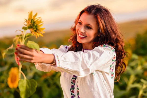 Beautiful woman enjoying nature in the sunflower field at sunset. Traditional clothes. Attractive brunette woman with long and healthy hair.