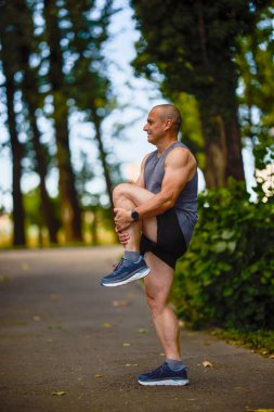Parktaki erkek sporcu, koşudan önce ısınıyor ve ısınıyor..