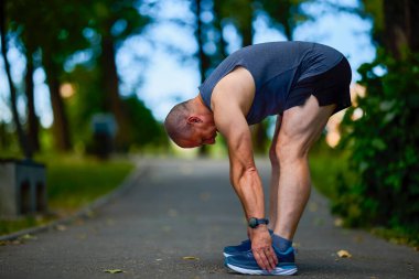 Parktaki erkek sporcu, koşudan önce ısınıyor ve ısınıyor..