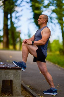 Parktaki erkek sporcu, koşudan önce ısınıyor ve ısınıyor..