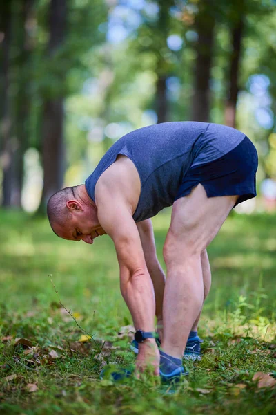 Parktaki erkek sporcu, koşudan önce ısınıyor ve ısınıyor..
