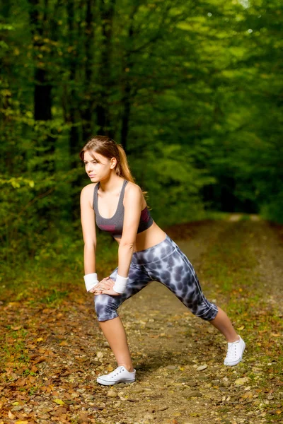 Belle jeune femme faisant des exercices d'étirement sur la forêt de la route — Photo