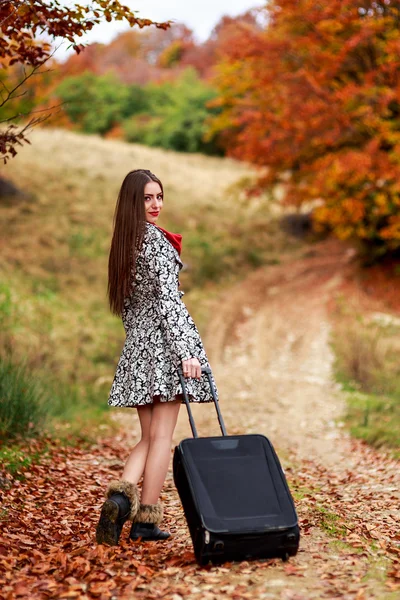 Menina bonita esperando em uma estrada de campo com sua mala . — Fotografia de Stock