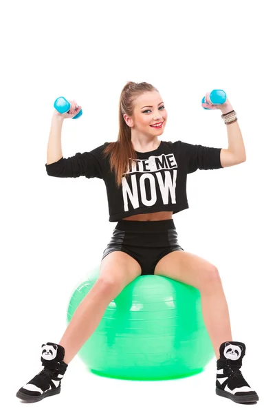 Jovem mulher desportiva sentado no fitball com halteres no branco ba — Fotografia de Stock