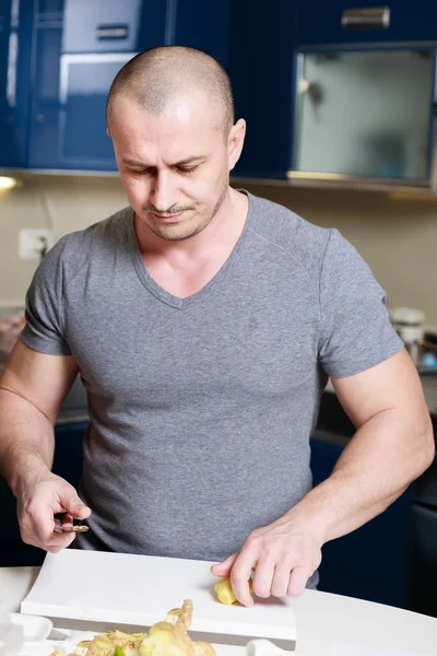 Bel homme qui épluche le gingembre sur une table dans la cuisine — Photo