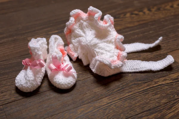 Baby's bootee and cap on wooden background — Stock Photo, Image