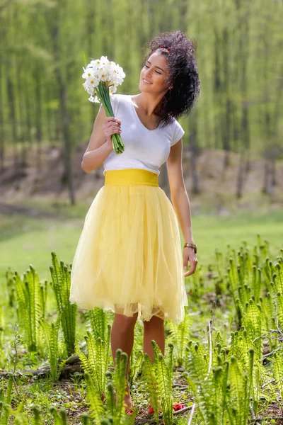 A beautiful young woman with a bouquet of daffodils in nature — Stock Photo, Image