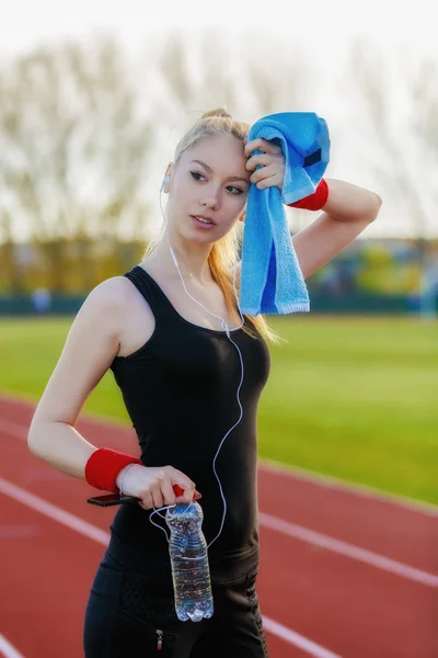 Joven mujer deportiva sosteniendo la botella de agua y limpiando el sudor con un — Foto de Stock