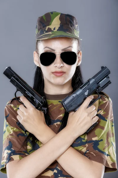 Soldatin in Tarnuniform mit Waffe auf grauem Hintergrund — Stockfoto