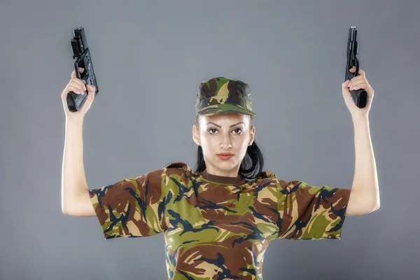 Soldatin in Tarnuniform mit Waffe auf grauem Hintergrund — Stockfoto