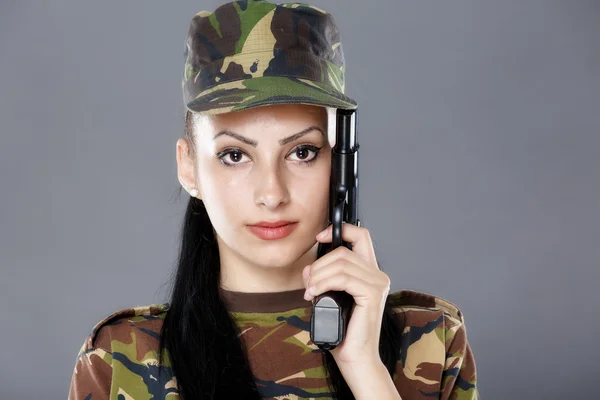 Soldatin in Tarnuniform mit Waffe auf grauem Hintergrund — Stockfoto