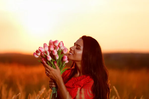 Piękna brunetka kobieta w czerwonej sukience z tulipany w ręce na — Zdjęcie stockowe