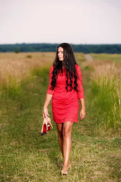 Beautiful brunette woman with shoes in hand on a field at sunset — Stock Photo, Image