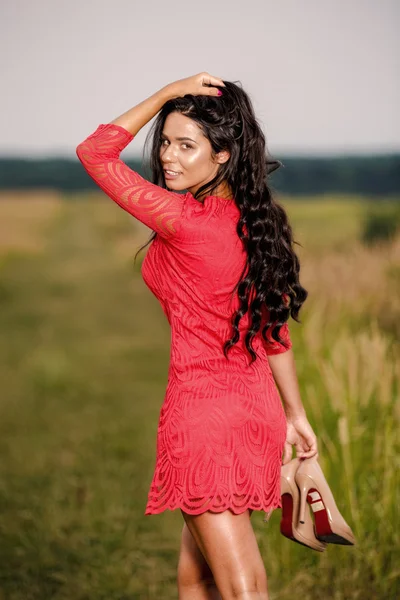 Beautiful brunette woman with shoes in hand on a field at sunset — Stock Photo, Image