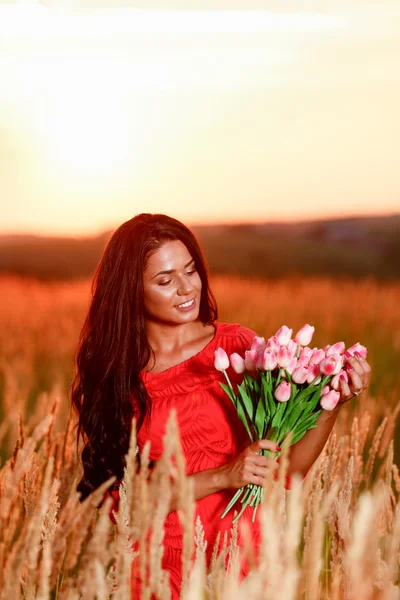Piękna brunetka kobieta w czerwonej sukience z tulipany w ręce na — Zdjęcie stockowe