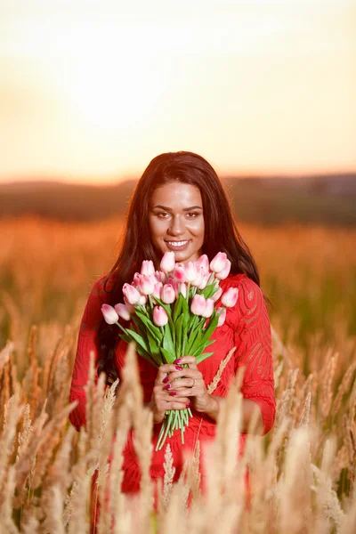 Bela mulher morena em vestido vermelho com tulipas nas mãos em um — Fotografia de Stock