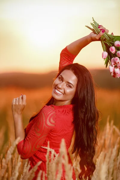 Schöne brünette Frau in rotem Kleid mit Tulpen in den Händen auf einem — Stockfoto