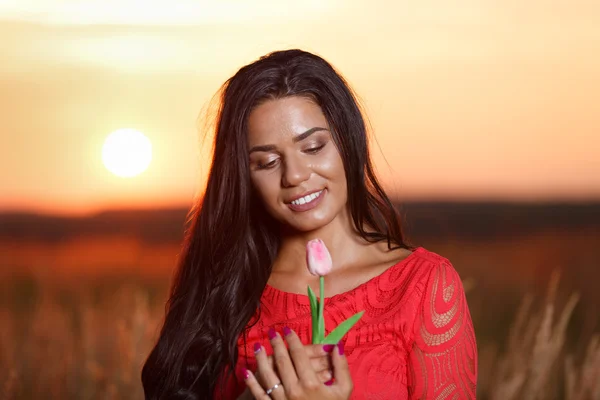 Beautiful brunette woman in red dress with tulips in hands on a — Stock Photo, Image