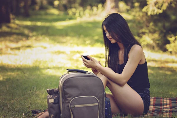 A beautiful young woman sitting at a picnic in nature and uses t — Stock Photo, Image