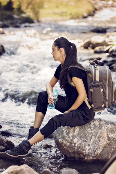 Beautiful woman resting on a rock in the river and drinking wate — Stock Photo, Image