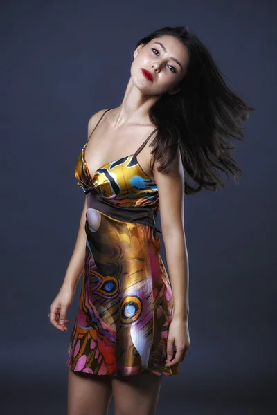 Young brunette lady in colour dress posing on grey background — Stock Photo, Image