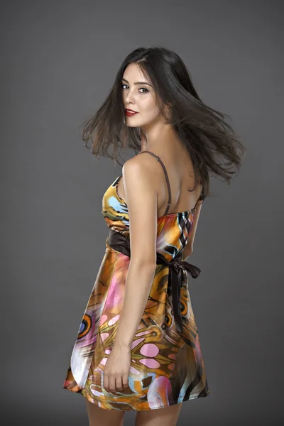 Young brunette lady in colour dress posing on grey background — Stock Photo, Image