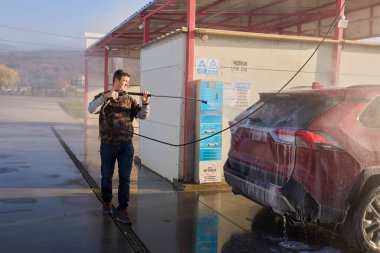 Orta yaşlı bir adam araba yıkamada arabasını yıkıyor.