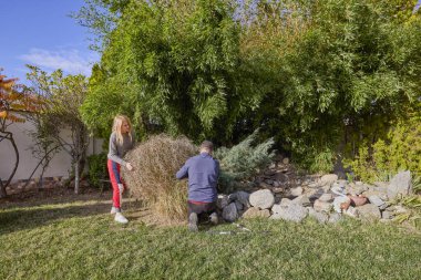Orta yaşlı bir adam ve karısı bahçede çalışıyor ve çeşitli bakım işleri yapıyorlar..