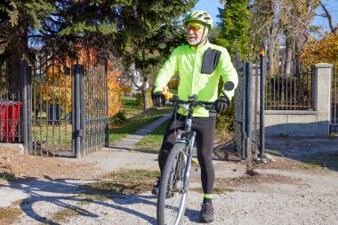 Yaşlı adam güzel bir sonbahar gününde bisiklet sürerek egzersiz yapıyor.