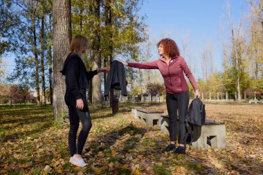 Orta yaşlı bir kadın arkadaşıyla parkta yürüyor, rahatlıyor, sohbet ediyor ve bir şeyler atıştırıyor..