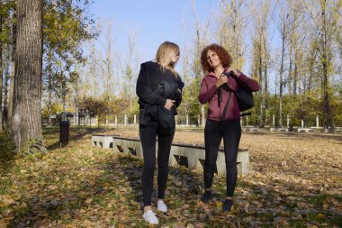 Orta yaşlı bir kadın arkadaşıyla parkta yürüyor, rahatlıyor, sohbet ediyor ve bir şeyler atıştırıyor..